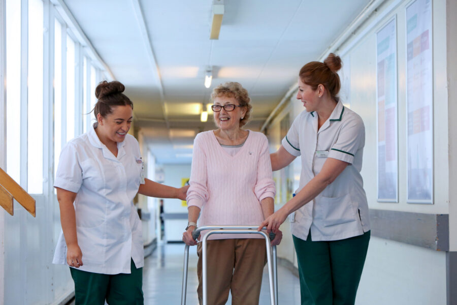 Two physios helping older woman with walking frame