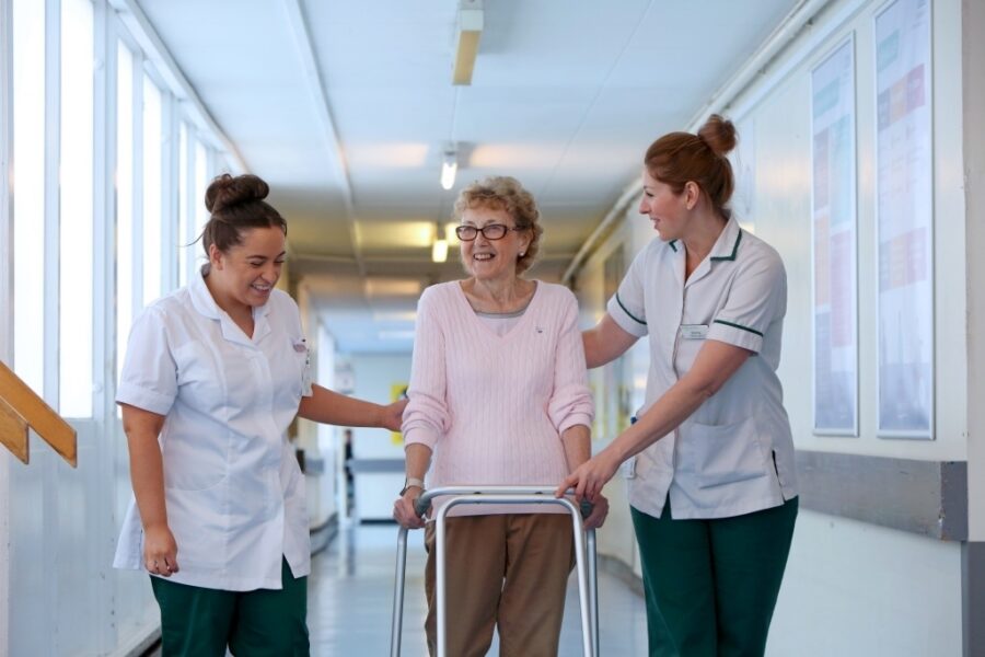Two therapists helping older patient with walking frame