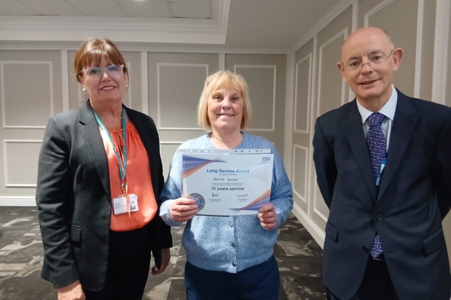 Three people, middle one holding award certificate